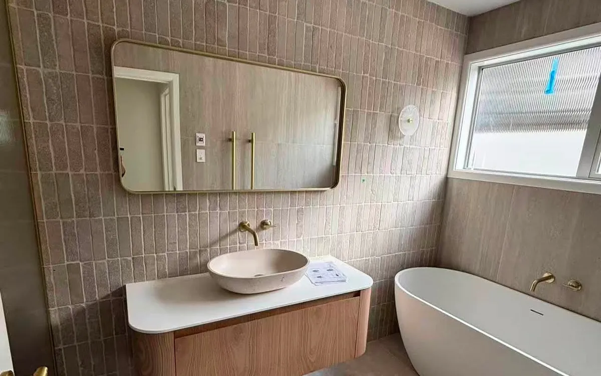 Finished bathroom with vertical stack tiling, a timber vanity, brass tapware and a freestanding bath